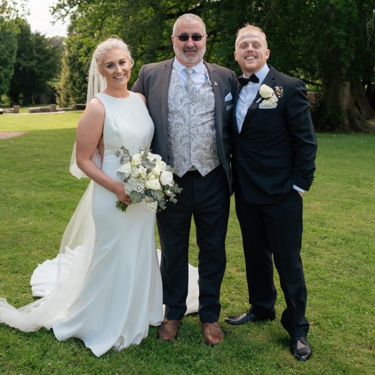 Wedding Ceremony Bride in a white dress, Groom in a dark suit with a Celebrant standing in the middle on a lawn