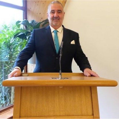 Funeral Celebrant behind Lectern Celebrant in a dark suit and blue tie standing behind a light varnished wooden lectern