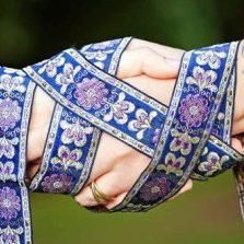 Handfasting Ritual Two hands palms clasped tied together with a blue, gold and pale white ribbon depicting a handfasting ritual